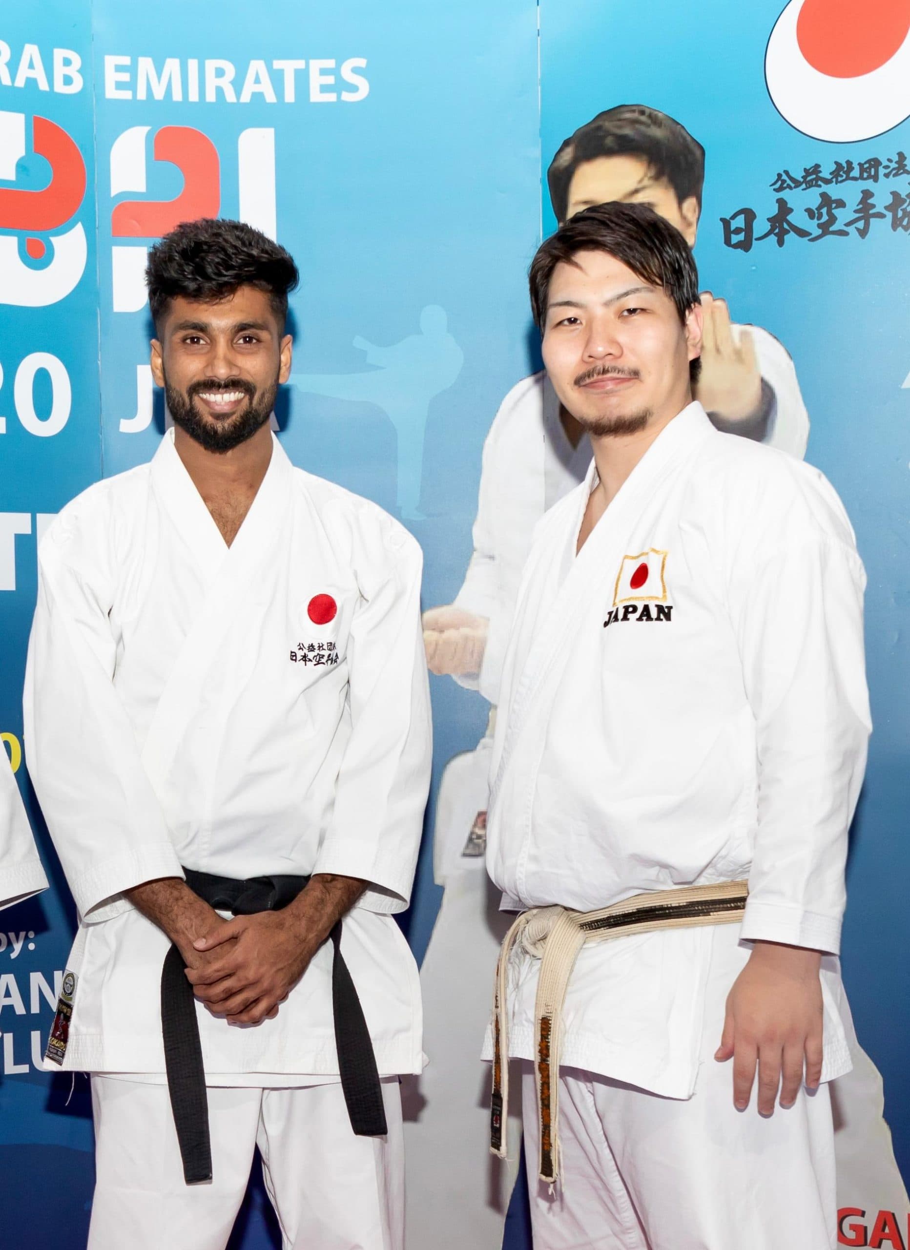 Two karatekas in Japan team gi posing in front of a JKA UAE event backdrop