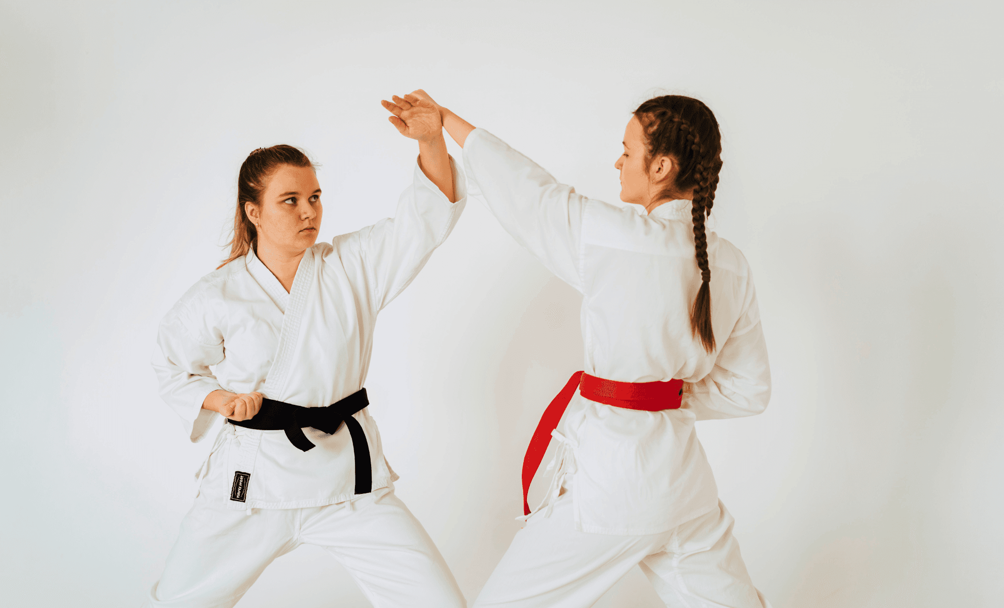 Two women in white gi practising a rising block against a straight punch in a bright studio