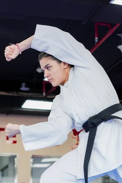 Female black belt performing an upper block with a clenched fist in a dojo