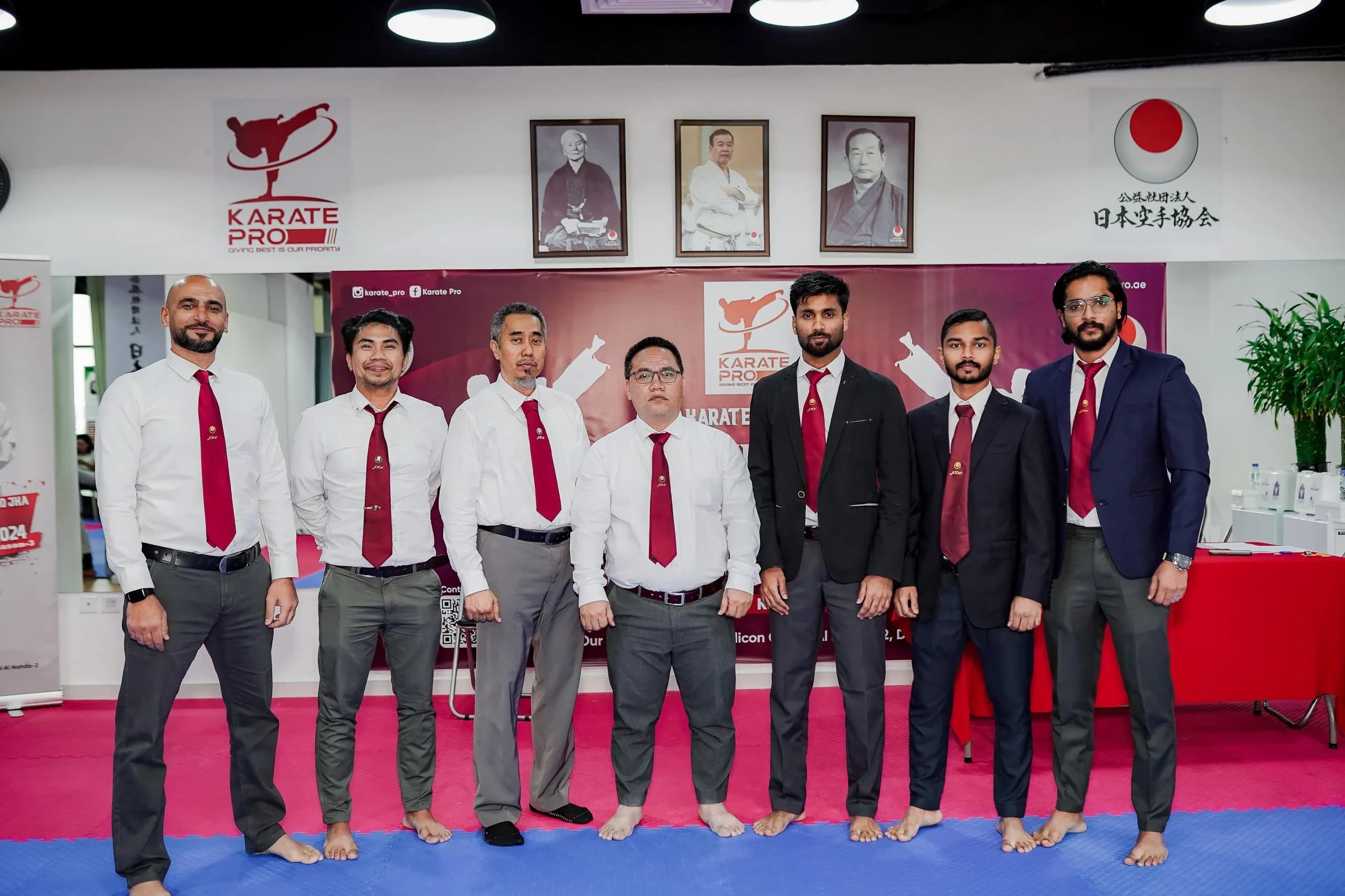 Karate Pro instructors and staff in white shirts and red ties lined up in front of the dojo wall
