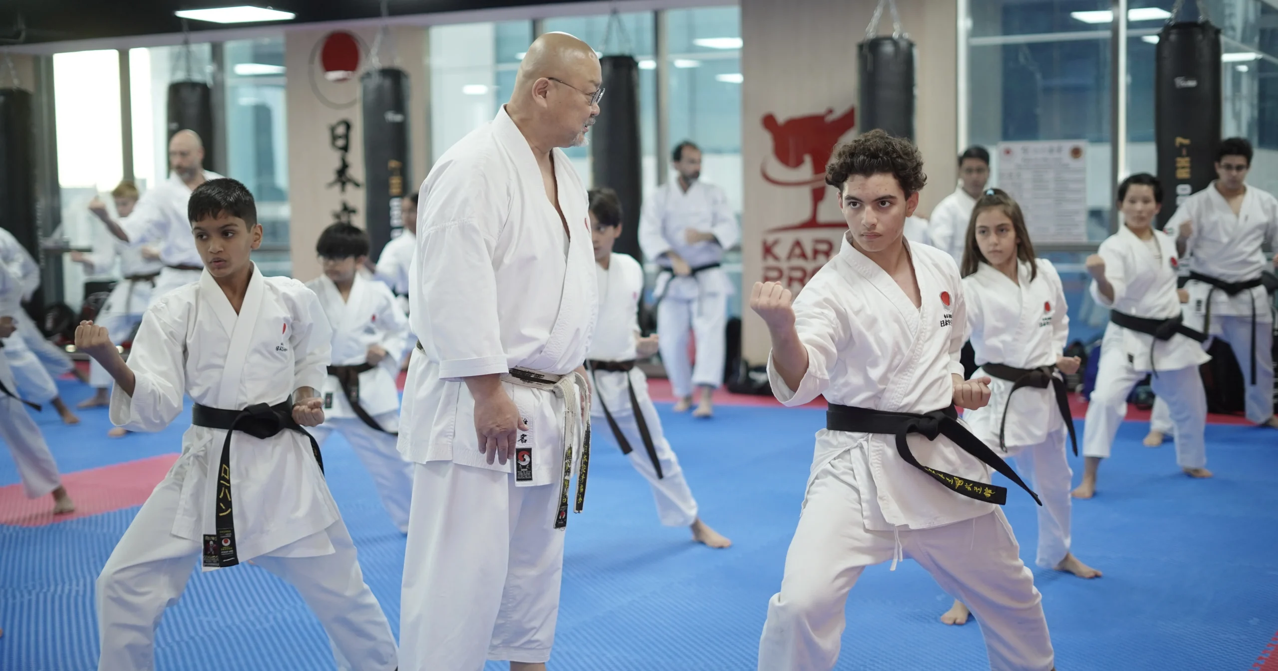 Instructor walking among black belt students as they hold a punching stance on the blue mats