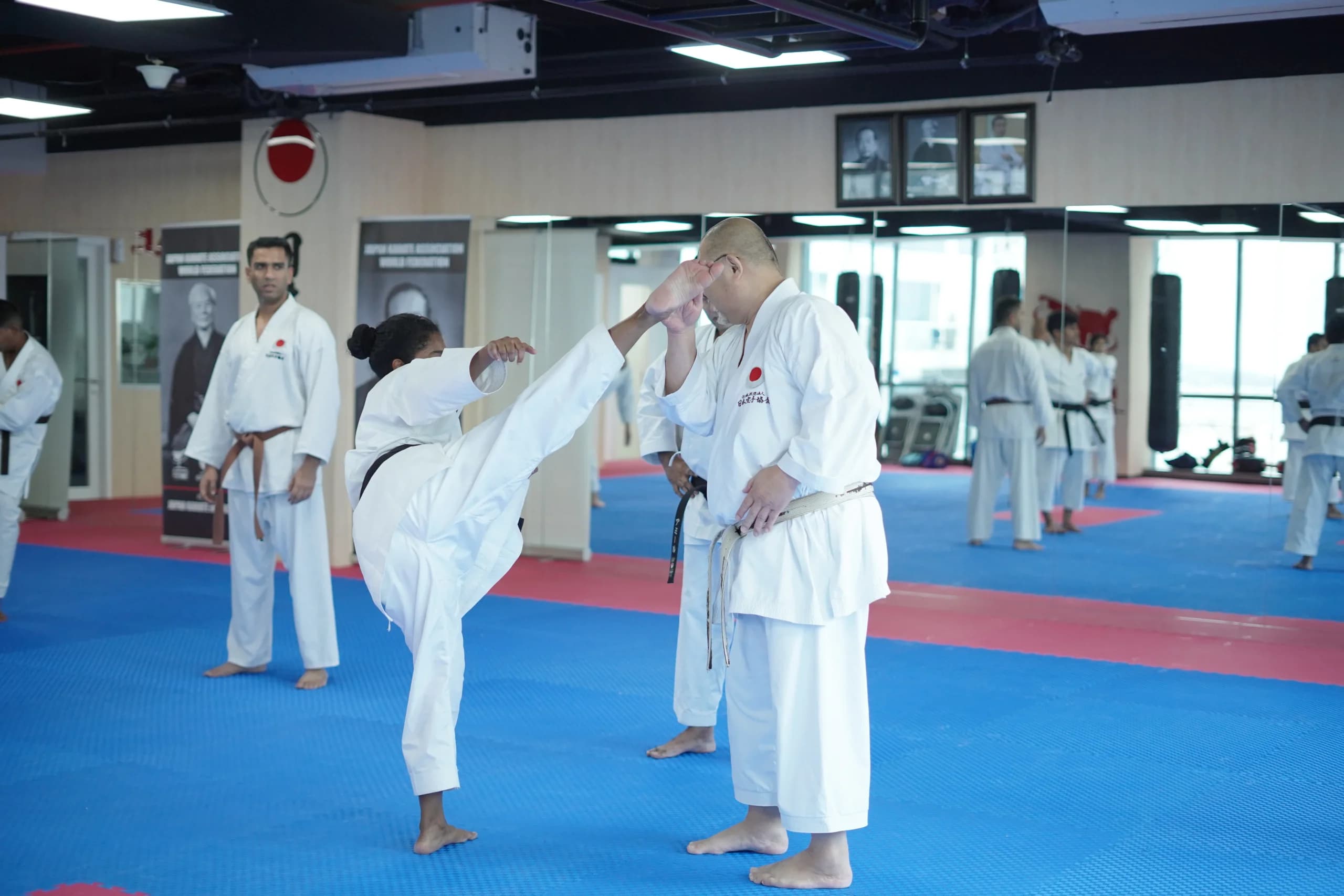 Adult black belt delivering a high roundhouse kick towards a training partner during class