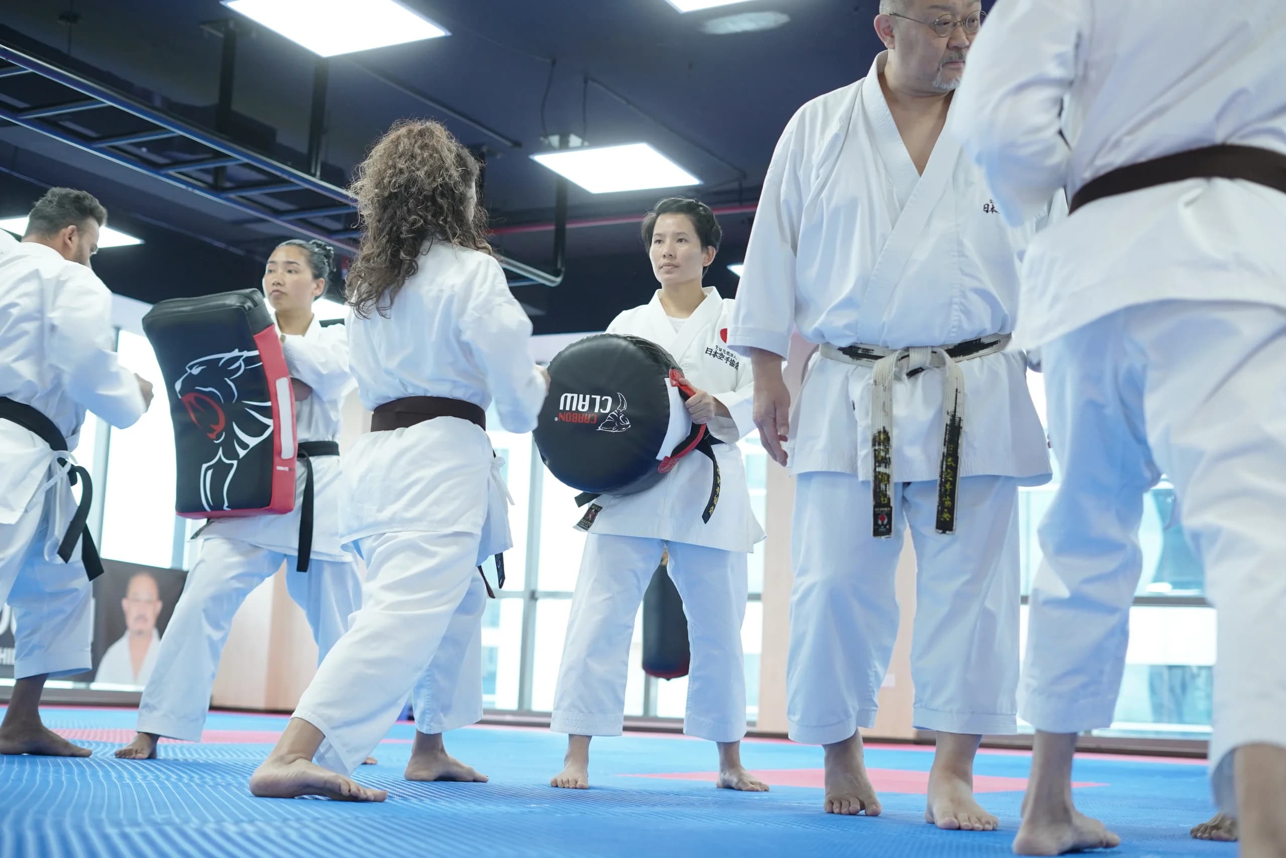 Adult students striking hand-held focus pads during a kicking drill in the dojo