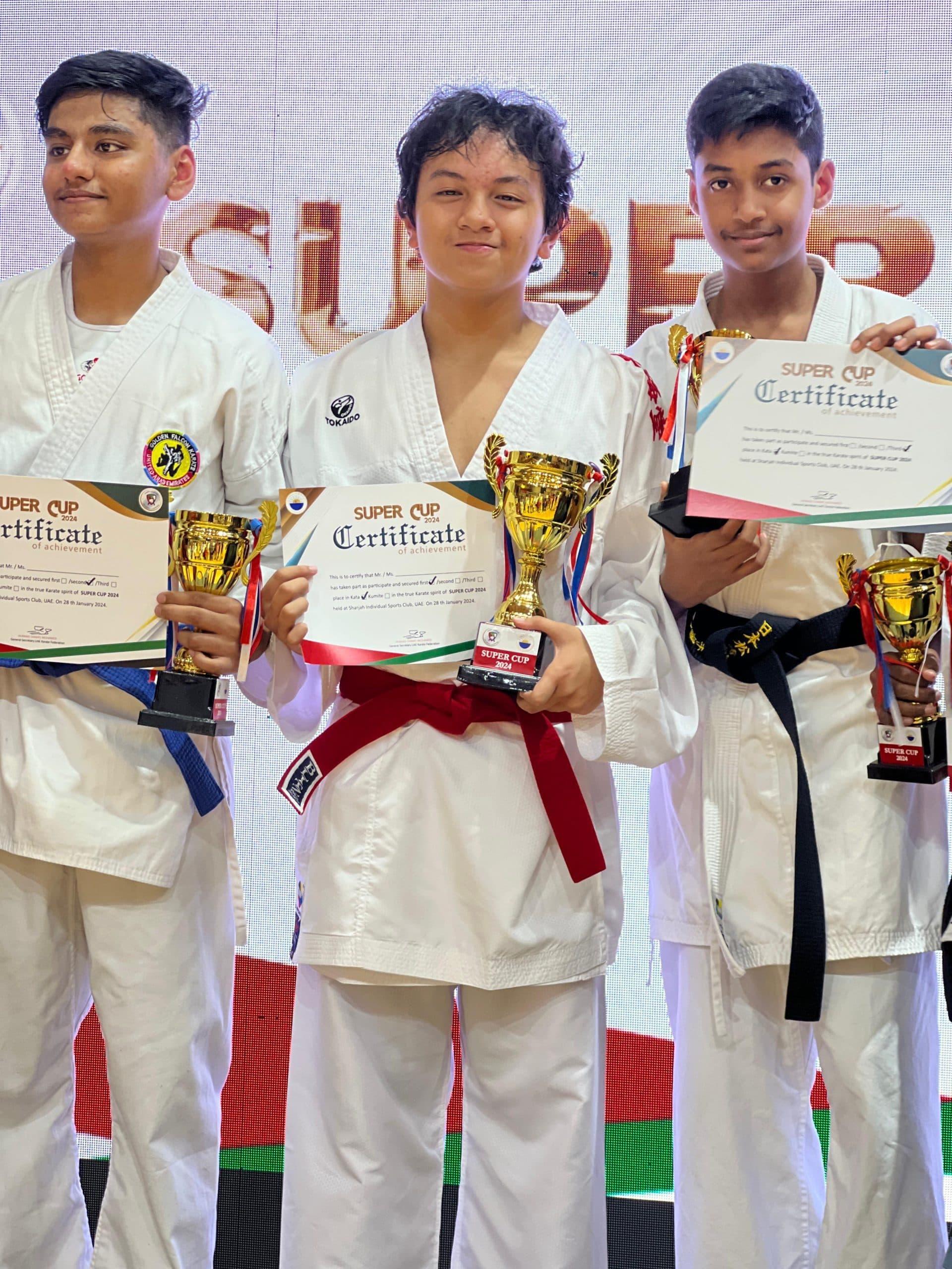 Three teenage boys holding trophies, medals and Super Cup certificates on stage