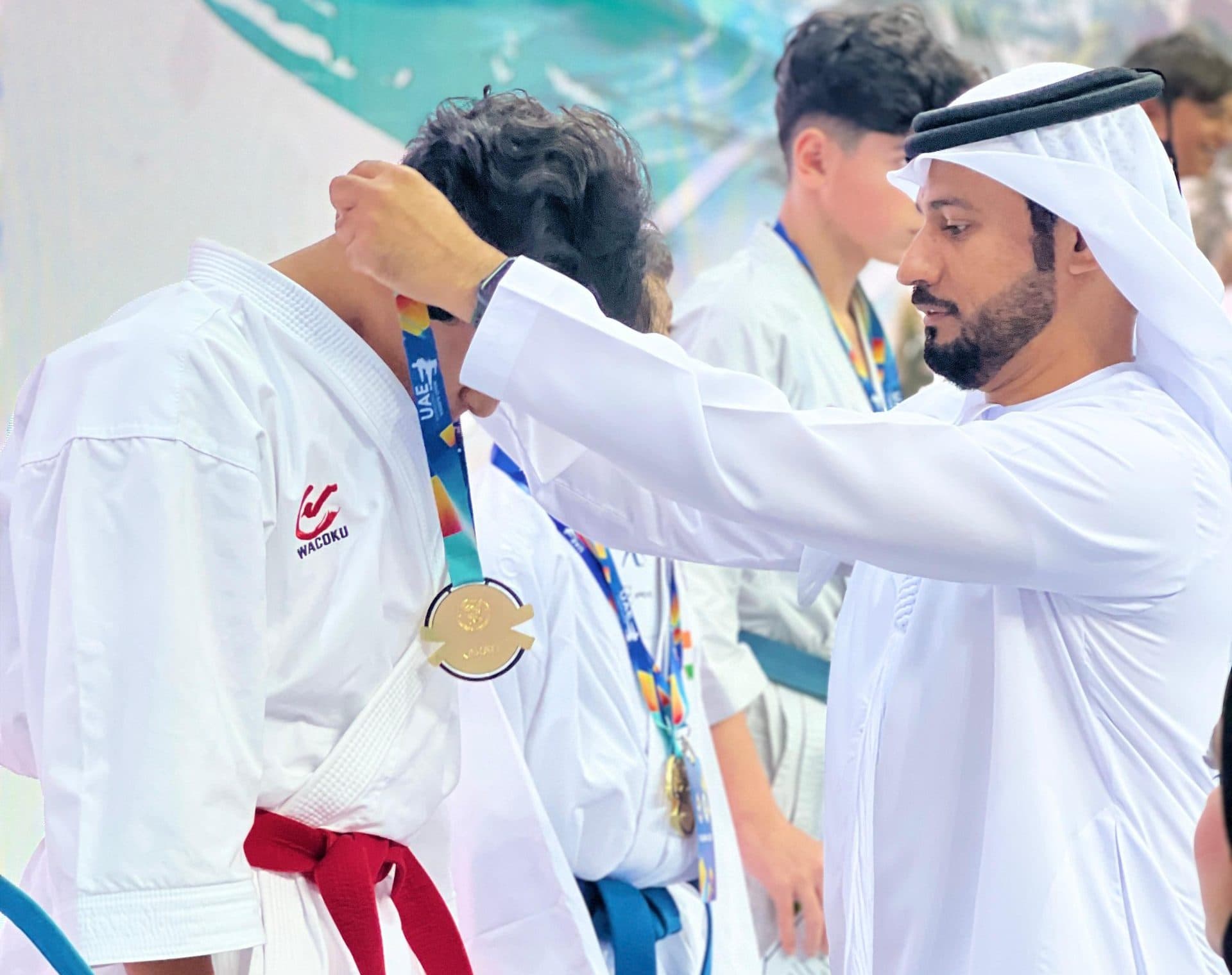Official in traditional Emirati dress placing a medal around the neck of a young competitor