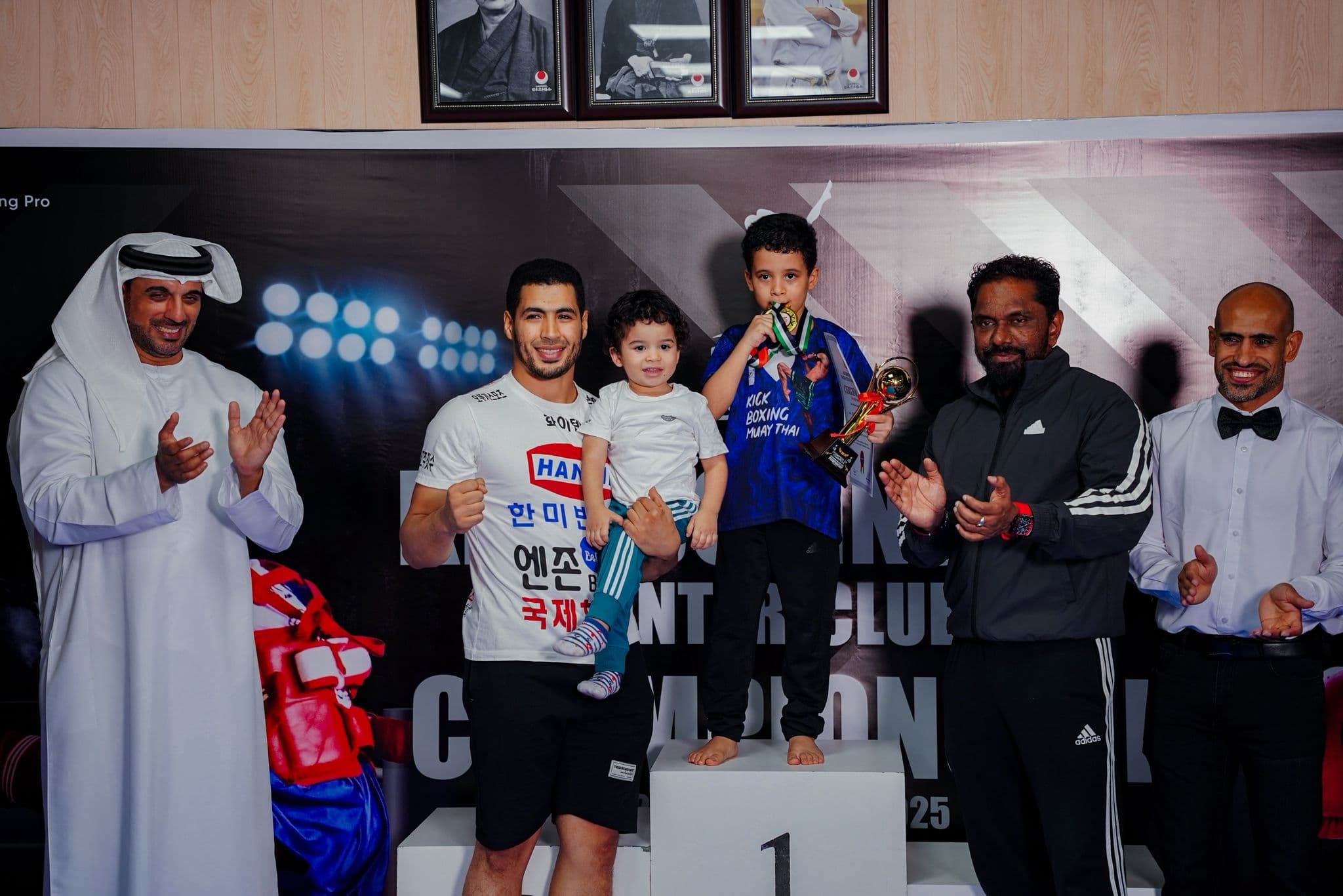 Young winner in a Karate Pro t-shirt holding a trophy on the podium at the Kickboxing pro inter club championship 2025