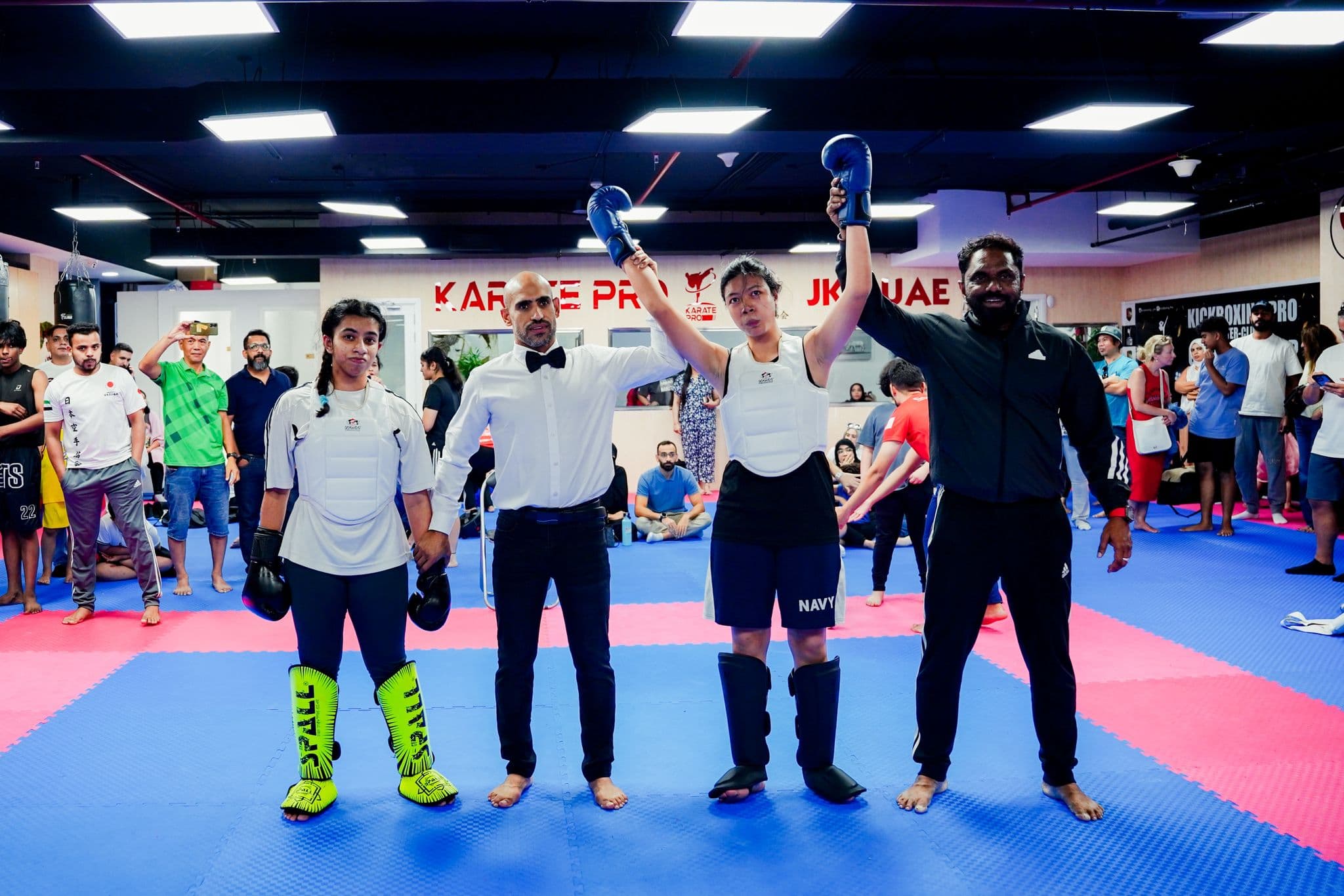 Referee raising the arm of the winning kickboxer beside her opponent after a bout