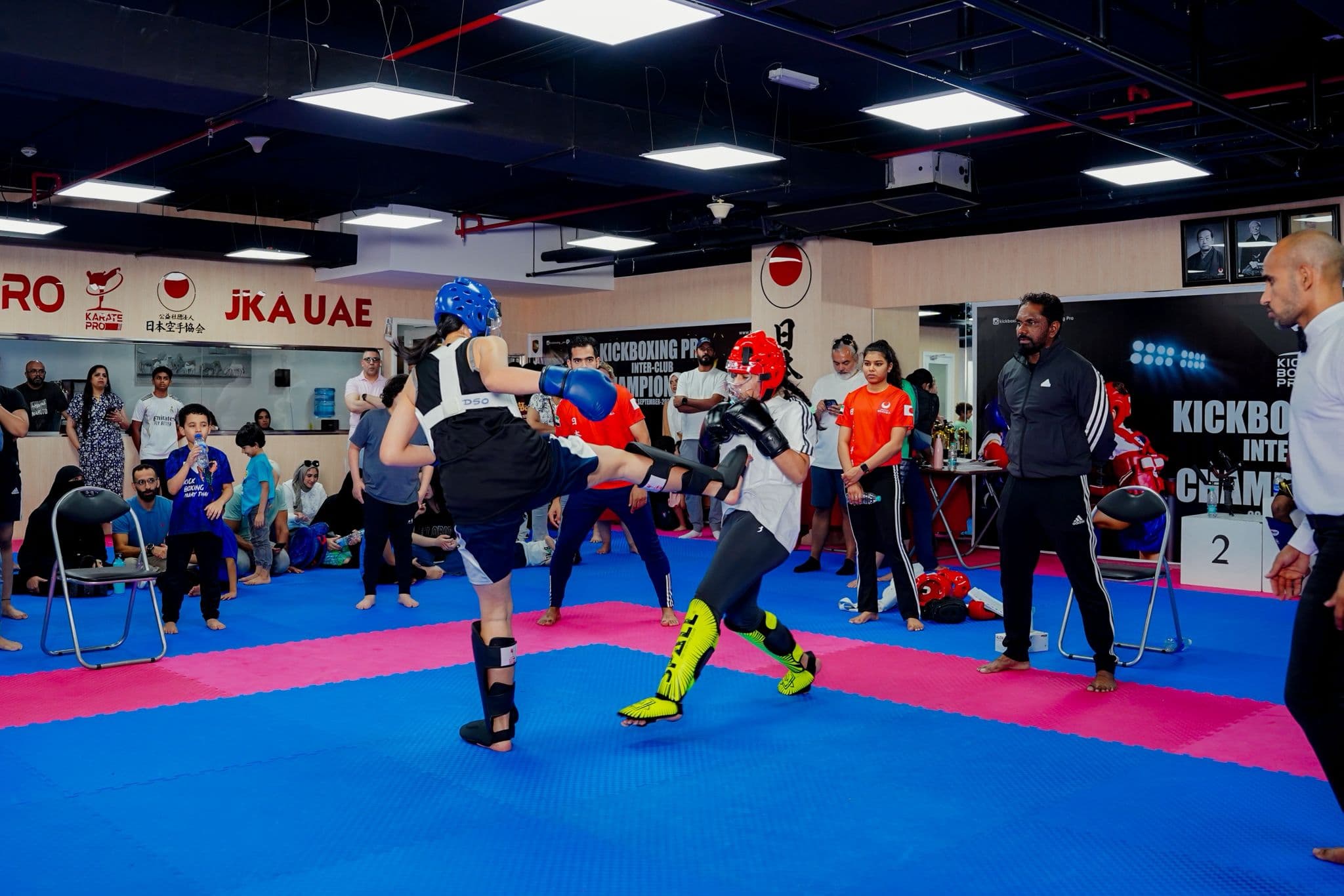 Kickboxer in blue head guard landing a high kick during a championship bout on the mats