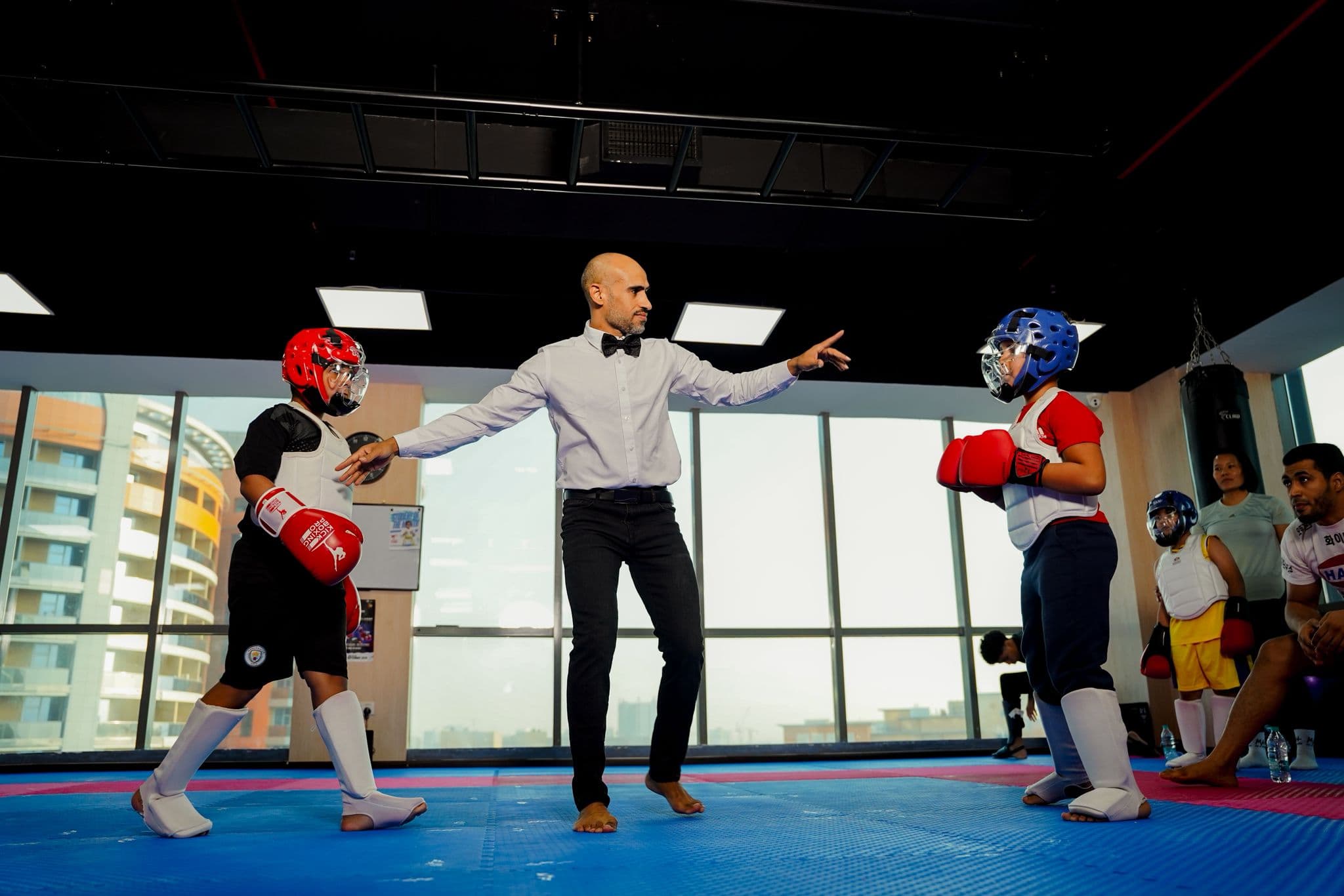 Referee separating two young kickboxers in red and blue head guards during a bout