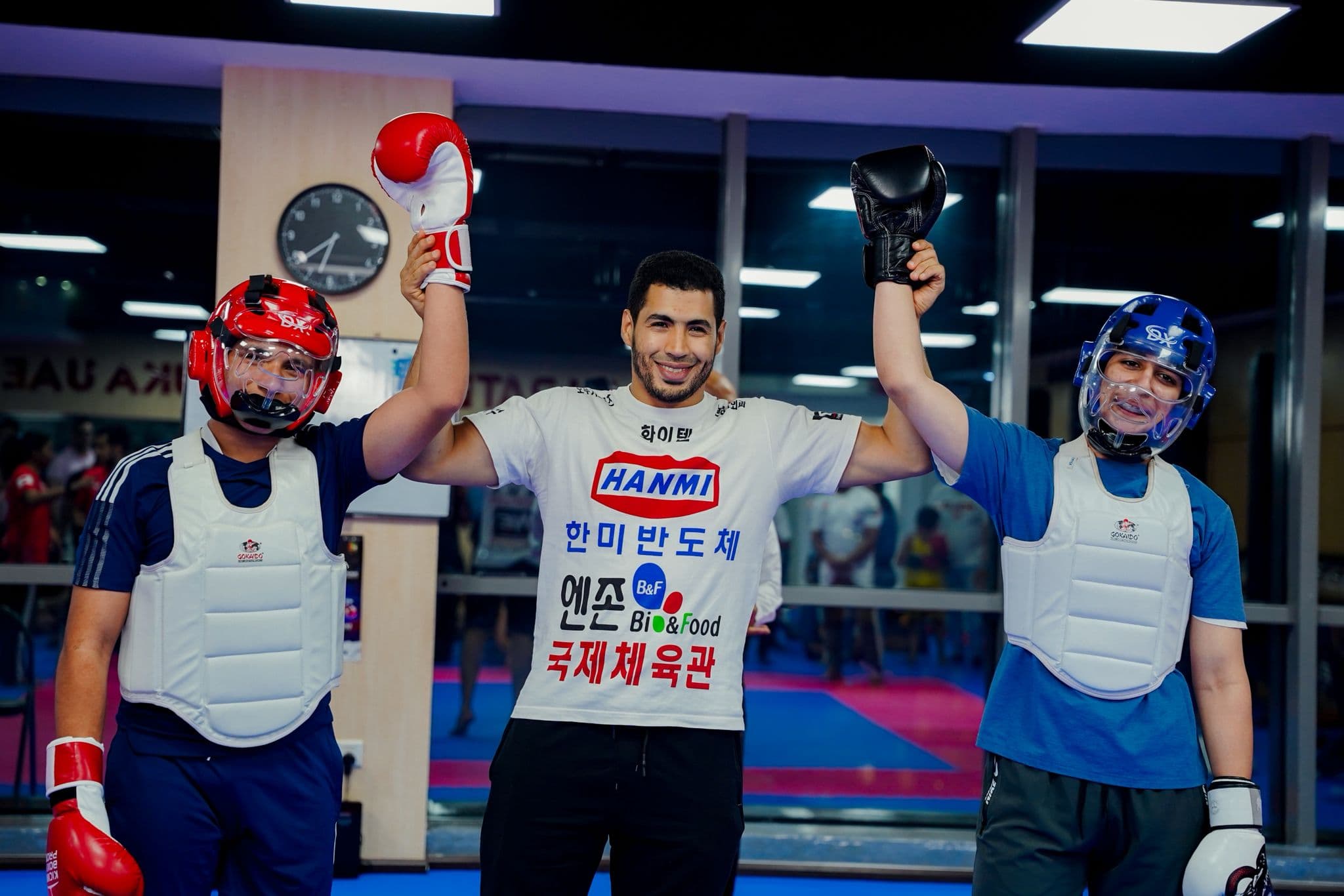 Referee raising the arms of two young kickboxers in red and blue body armour after their bout