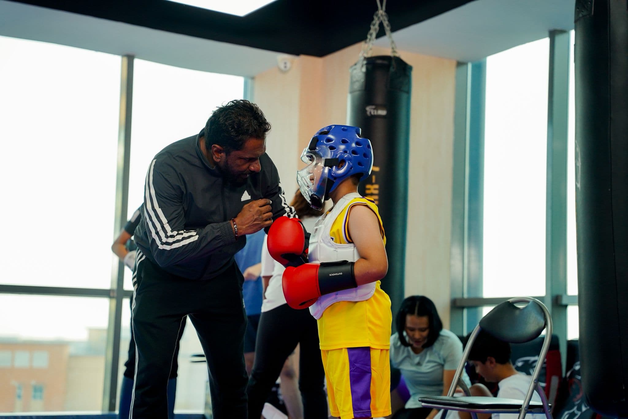 Coach adjusting a young competitor's head guard and gloves before a kickboxing bout