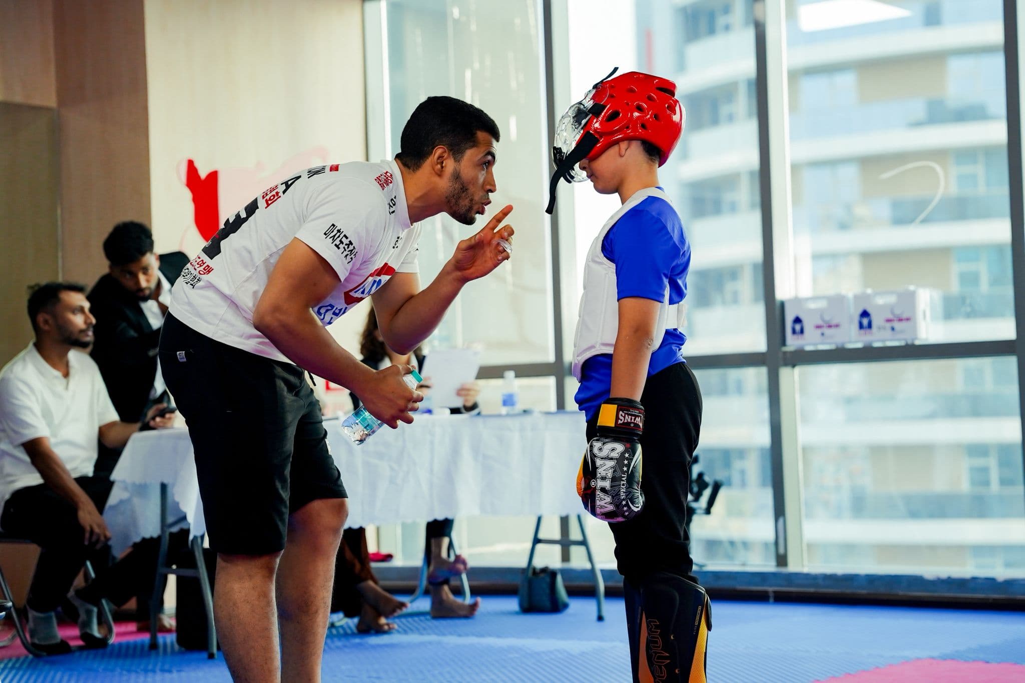 Coach giving last-minute instructions to a young kickboxer in a red head guard