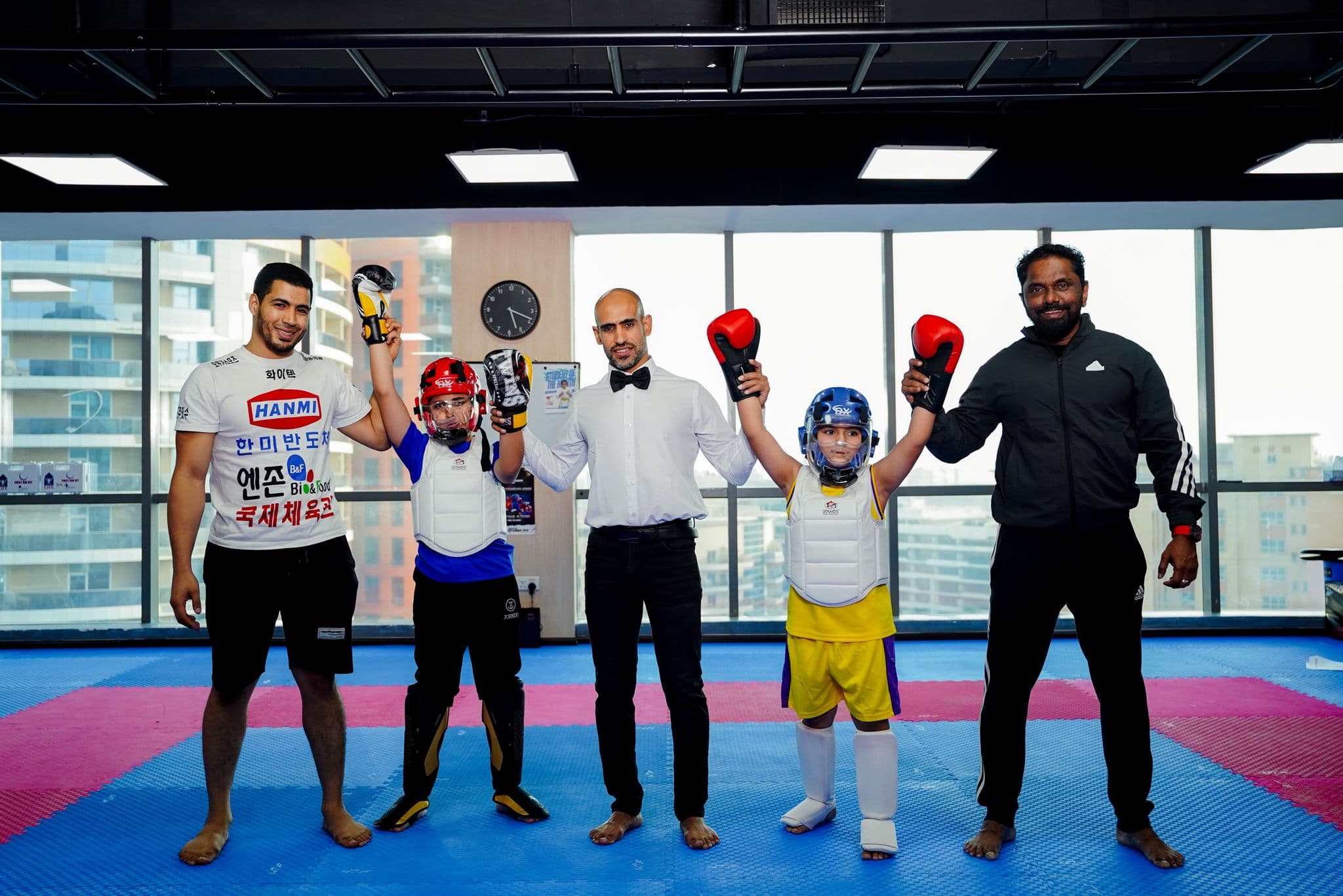 Referee raising the arm of a young winner in yellow shorts as the opponent and coaches look on