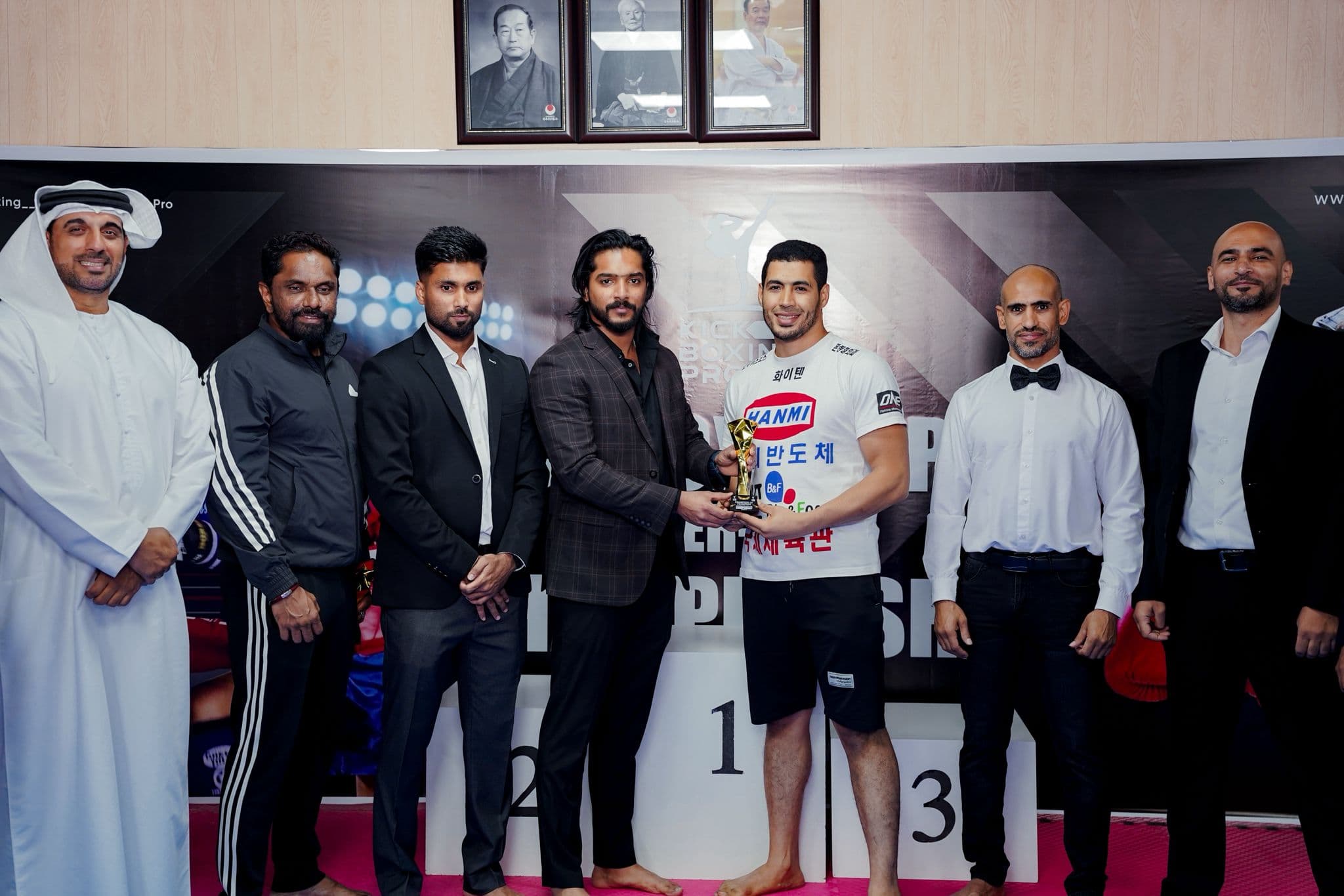 Champion holding a trophy on the podium surrounded by officials at the Kickboxing pro inter club championship 2025
