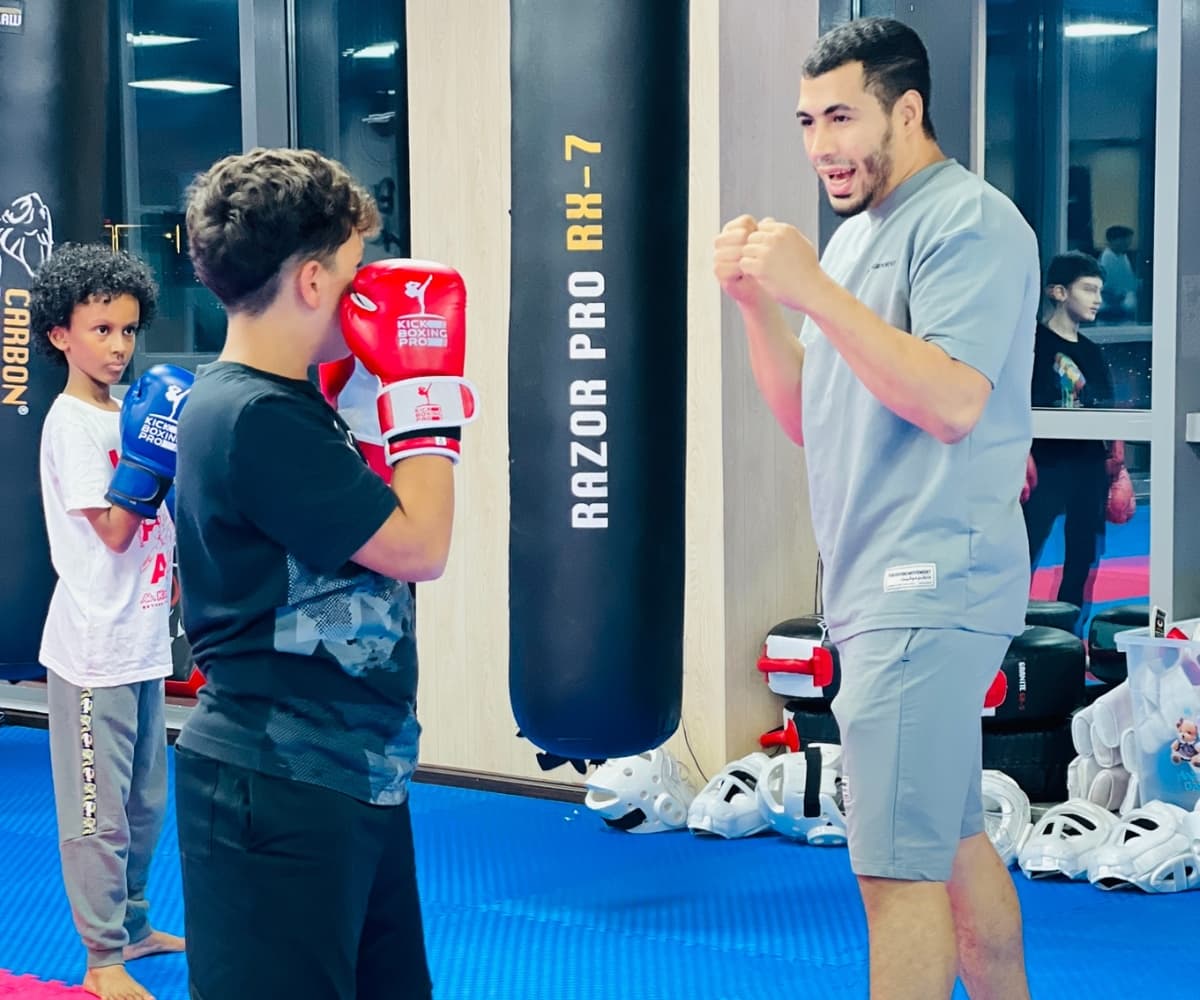 Coach guiding a young student's guard beside the heavy bags in the dojo