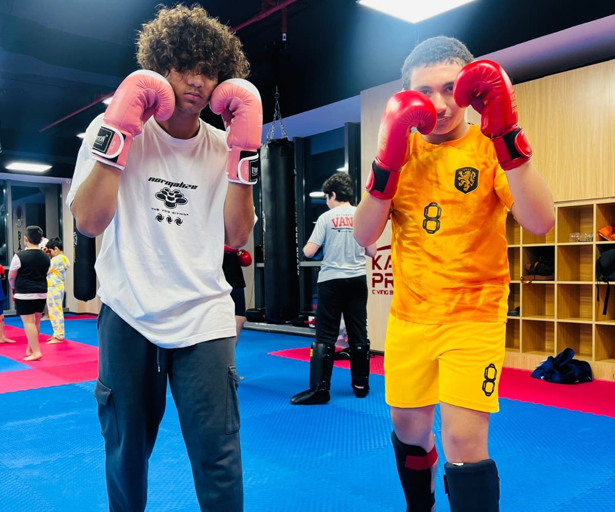 Two teenage boys in red gloves holding high guards during a kickboxing class
