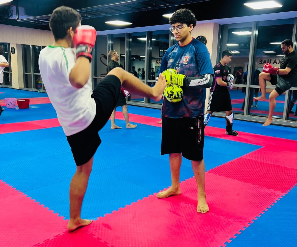 Teenager throwing a high kick towards a partner's mitt in the kickboxing class