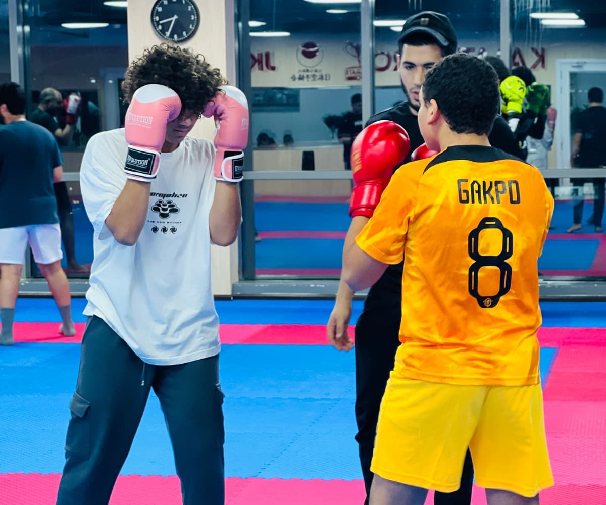 Two teenagers in gloves shadow boxing side by side while others train in the background