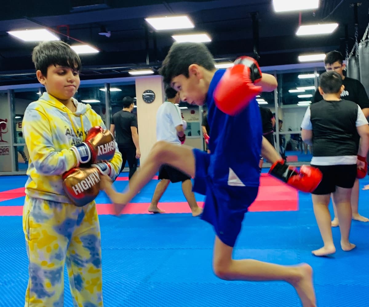 Young student in blue throwing a knee towards a partner's pads during class