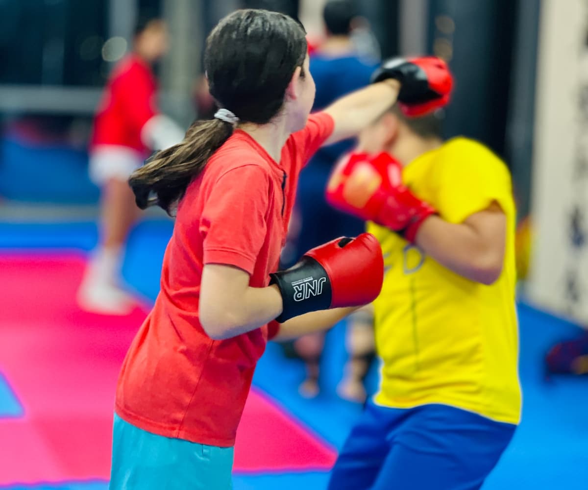 Girl in red t-shirt and gloves landing a punch on a partner's glove during a pad drill