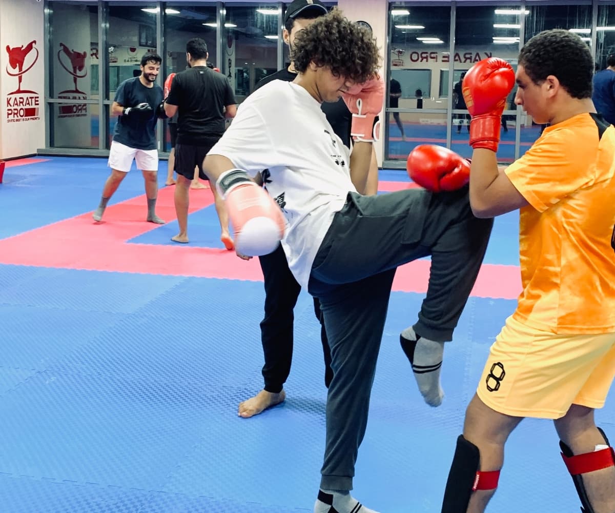 Teenager in white t-shirt landing a high kick on a partner in orange during sparring