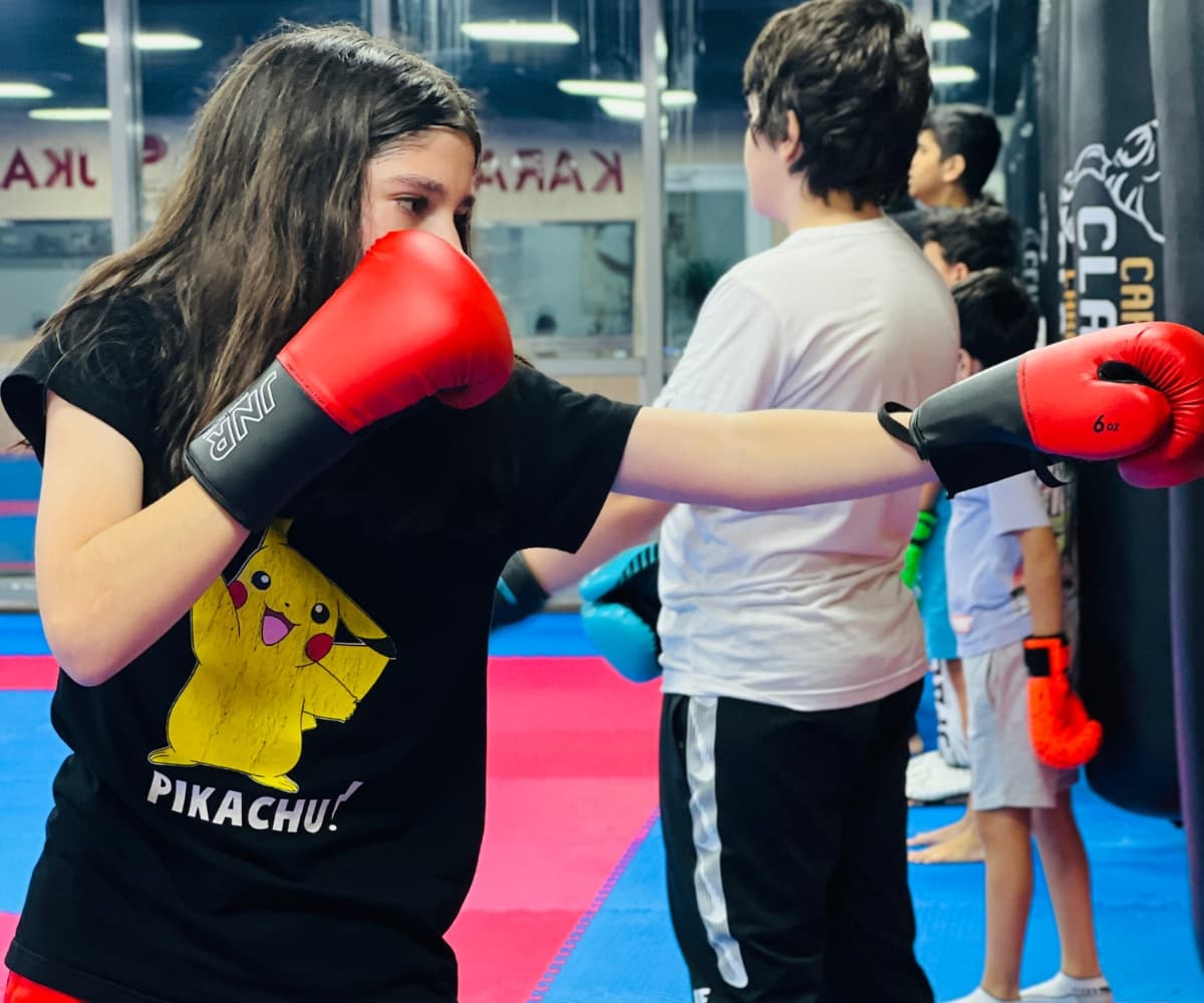 Young girl in a Pikachu t-shirt and red gloves practising a jab with a partner