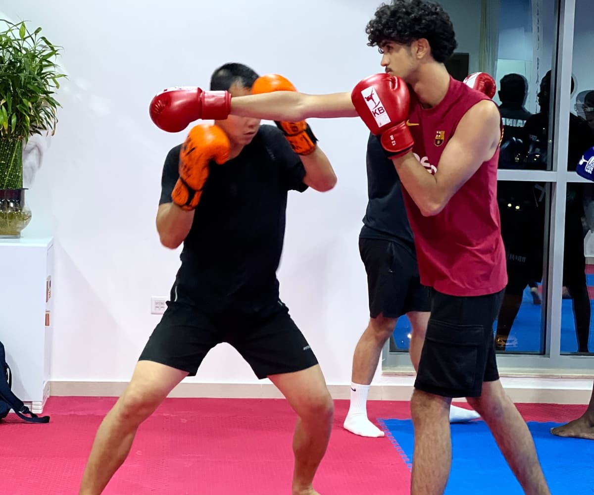 Two teenagers in gloves exchanging punches during a partner drill by the dojo windows