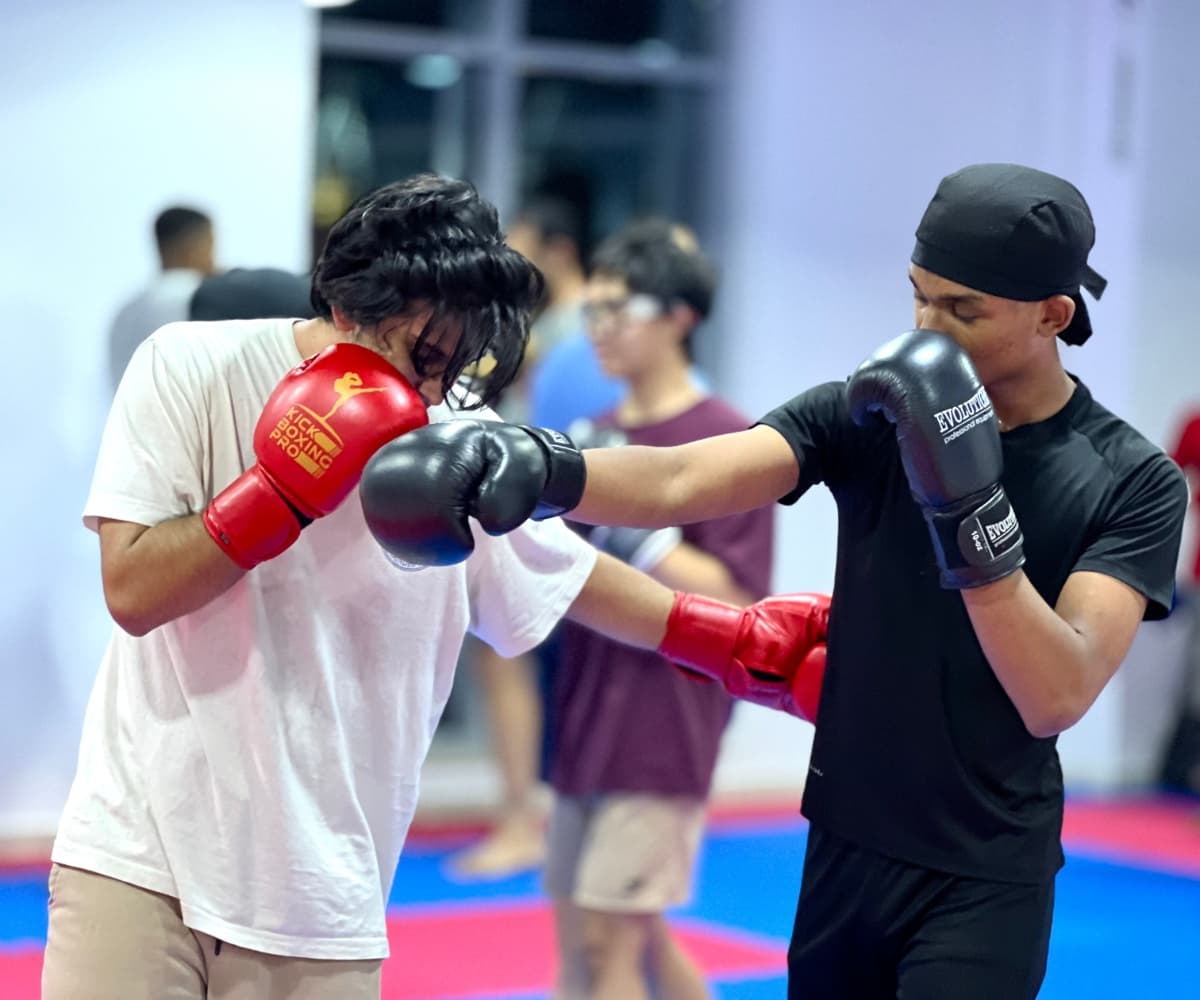 Two young kickboxers in gloves and one in a bandana trading punches during class