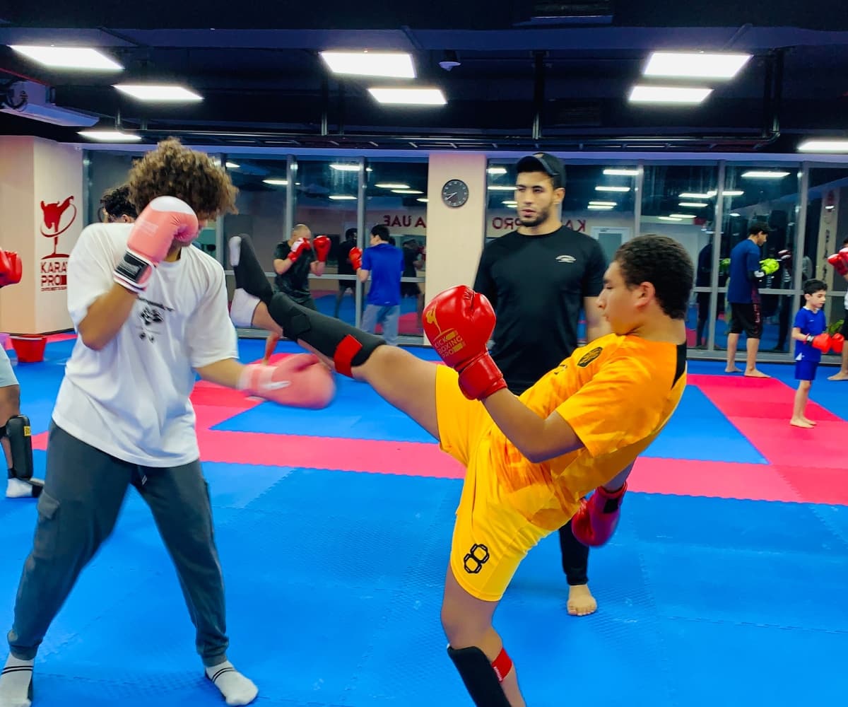 Teenager in orange kit throwing a high kick during a busy kickboxing class