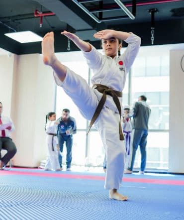 Young student in brown belt delivering a high kick in the dojo