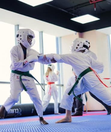 Two young students in head guards exchanging a punch and block during sparring practice