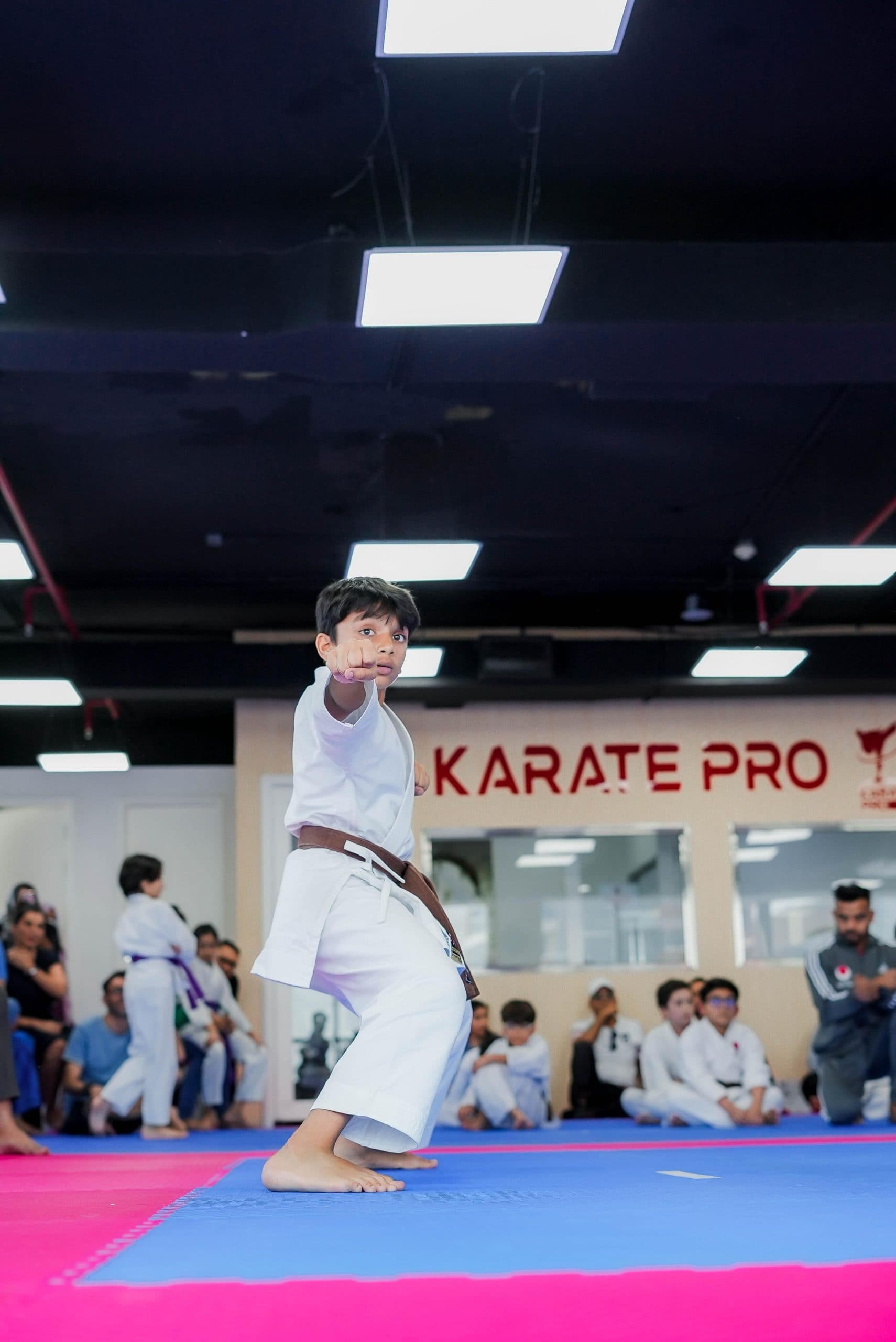 Young boy in brown belt punching during kata beneath the Karate Pro sign