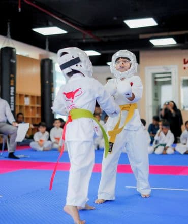 Two young students in head guards and body armour sparring on blue mats