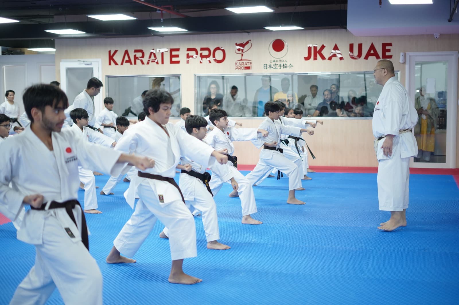 Teens and young adults practising a stance drill in rows beneath the Karate Pro and JKA UAE signage