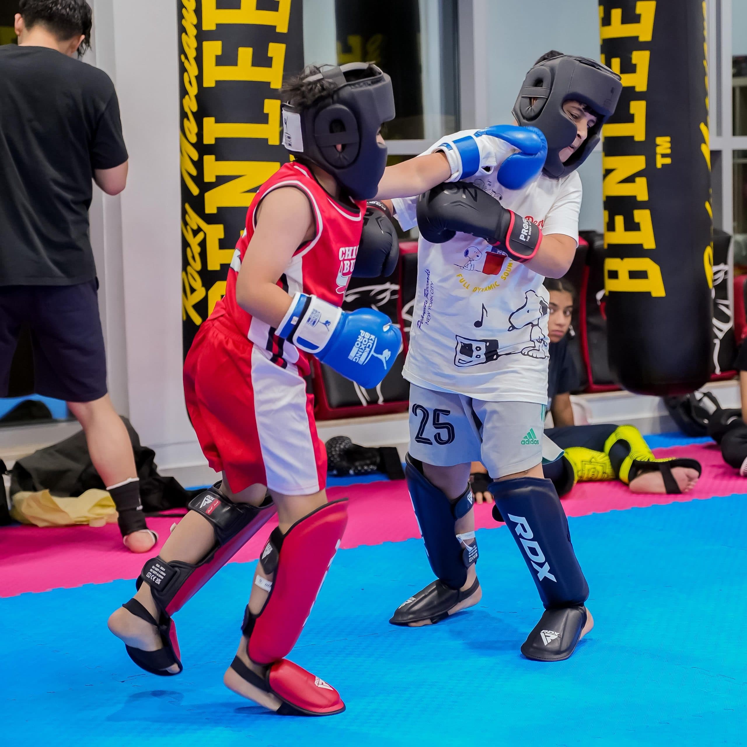 Two young kickboxers sparring in head guards on the mats