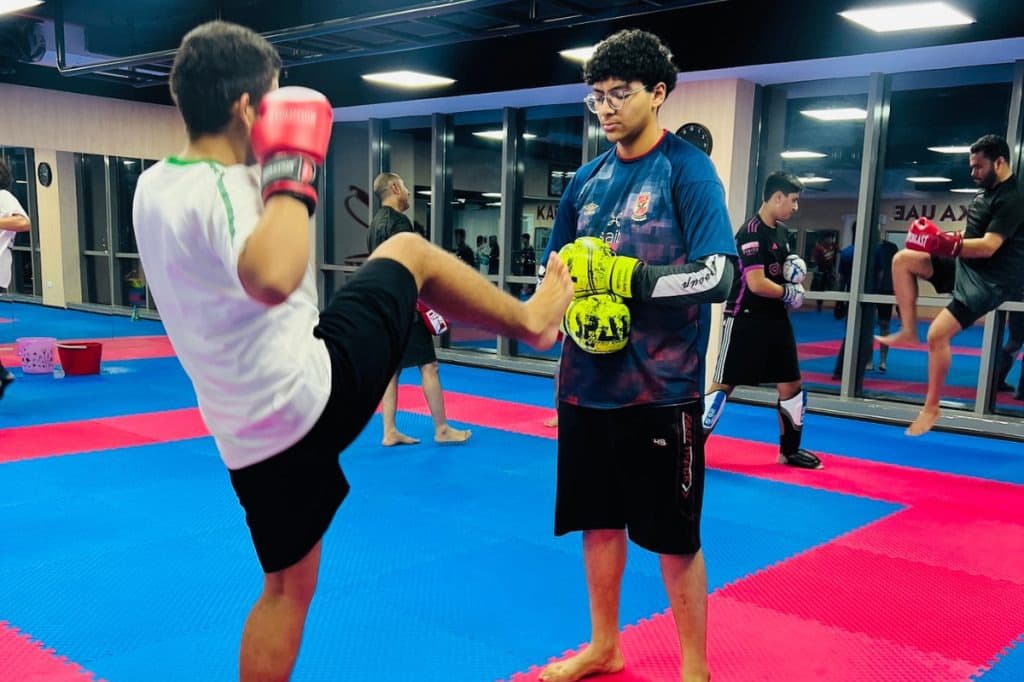 Young boy practising a kick on a coach's pad