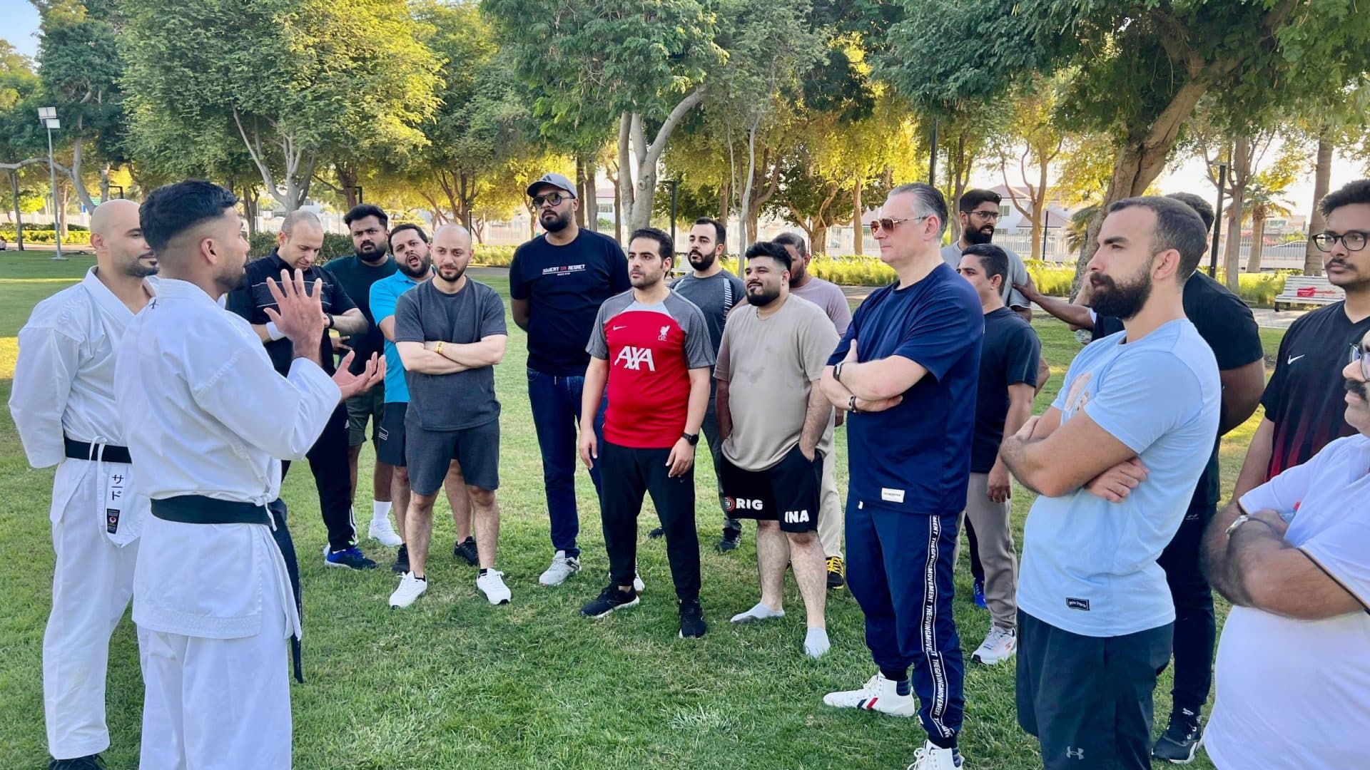 A Karate Pro coach in white gi leading an outdoor training session for a community group in a park