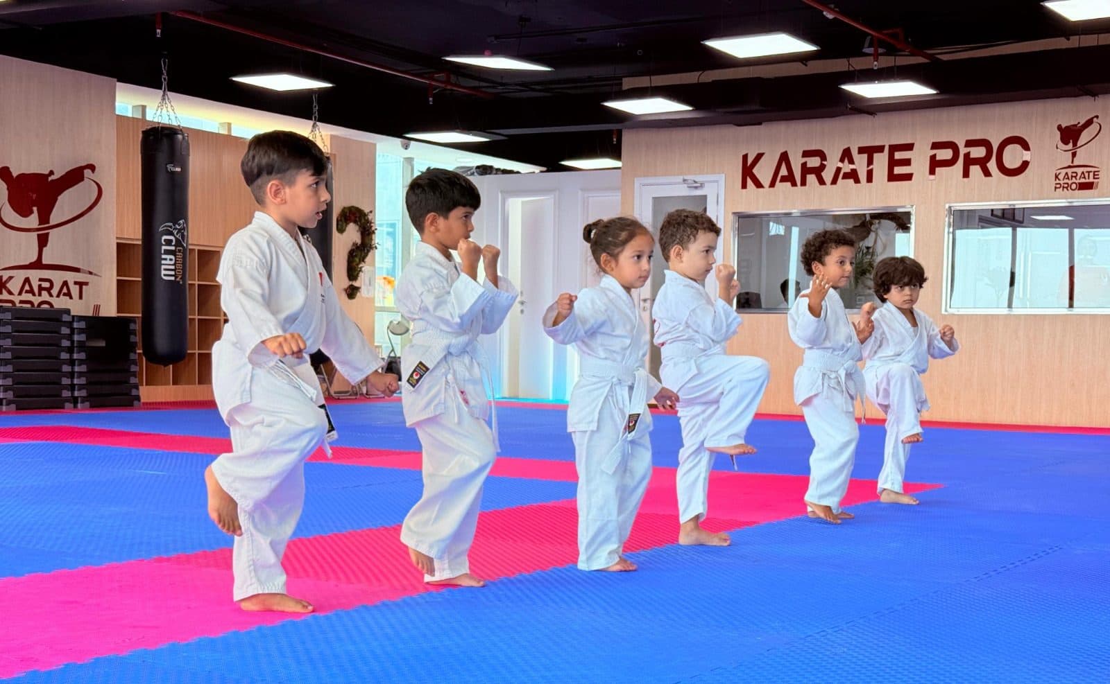 Young children in white gi practising front kicks together on the mats at Karate Pro Academy
